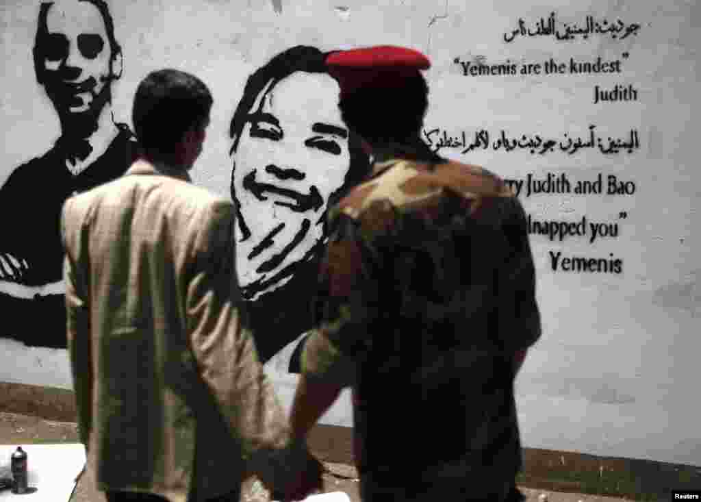 A soldier and a man look at a graffiti depicting kidnapped Dutch journalist Judith Spiegel (C) and her partner Boudewijn Berendsen in Sana&#39;a, Yemen. The couple were abducted in mid-June and are still held hostage by their kidnappers.