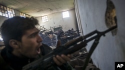 In this Saturday, December 15, 2012 photo, Free Syrian Army fighters aim their weapons as they chant religious slogans during heavy clashes with government forces at a military academy besieged by the rebels north of Aleppo, Syria. 