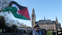 Seorang pedemo melambaikan bendera Palestina di luar Istana Perdamaian di mana Mahkamah Internasional berkantor di Den Haag, Belanda, 26 Januari 2024. (Foto: Patrick Post/AP Photo)