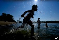 FILE - Judah Boyle, of Des Moines, Iowa, splashes water as he runs on the beach at Gray's Lake Park, Monday, Aug. 26, 2024, in Des Moines, Iowa. (AP Photo/Charlie Neibergall)