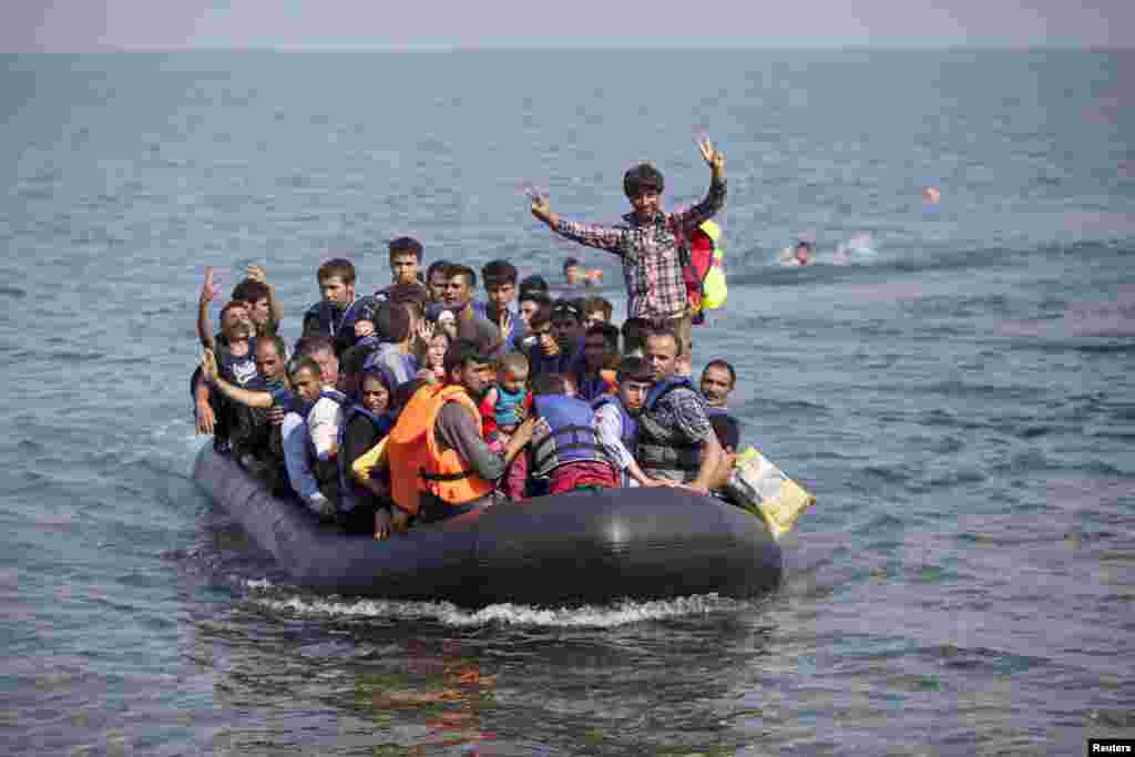 Syrian and Afghan refugees on a dinghy wave as they approach the Greek island of Lesbos, Sept. 3, 2015. The International Organization for Migration (IOM) says 1,500-2,000 are taking the route through Greece, Macedonia and Serbia to Hungary every day and that there is &quot;a real possibility&quot; the flow could rise to 3,000 daily.