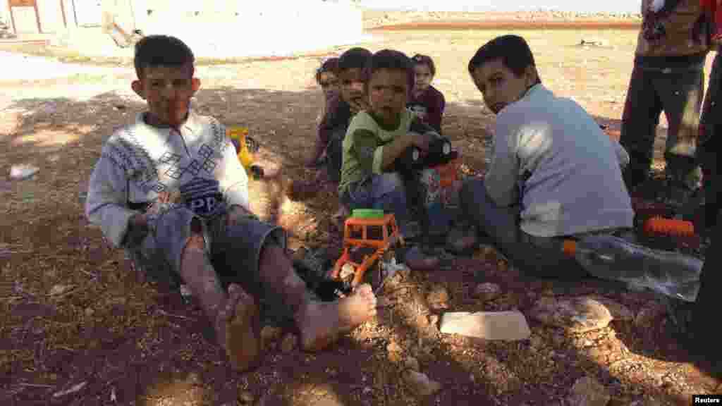 Syrian children, including a boy (L) injured during clashes between the Syrian Army and rebels, play with toys on the Syrian side of the border with Turkey, near Idlib, after having fled the violence in their town, October 13