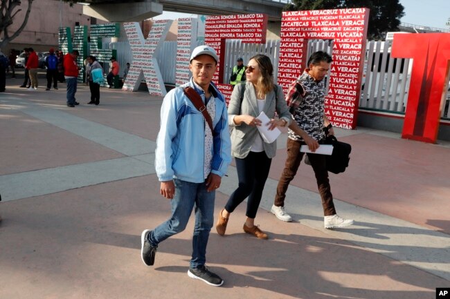 FILE - Two men, both of Honduras, walk with attorneys as they cross into the United States to begin their asylum cases, March 19, 2019, in Tijuana, Mexico.