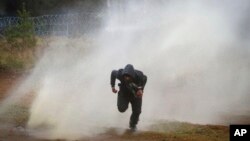 A man runs away from a water cannon during clashes between migrants and Polish border guards at the Belarus-Poland border near Grodno, Belarus, Nov. 16, 2021. 