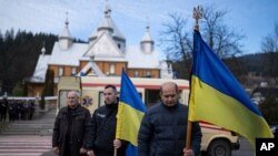 Personas sostienen banderas ucranianas durante la ceremonia fúnebre de los asesinados Vasyl Medviychuk y Dmytro Dosiak en las oficinas del ejército ucraniano en Verkhovyna, Ucrania, el jueves 28 de diciembre de 2023. (Foto: Archivo/AP)