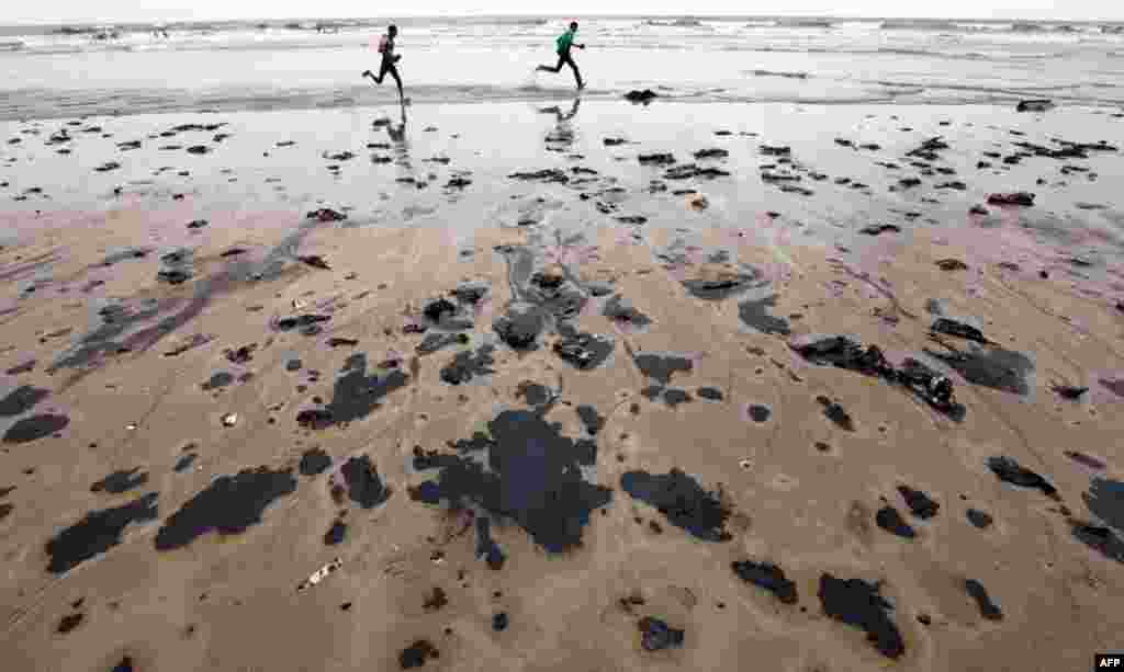 August 7: People play on the Juhu beach contaminated by oil leaking from a merchant ship that sank off the Arabian Sea coast in Mumbai, India. The 740-foot vessel was estimated to be carrying about 325 tons of fuel oil and 56 tons of diesel. (AP Photo/Ra