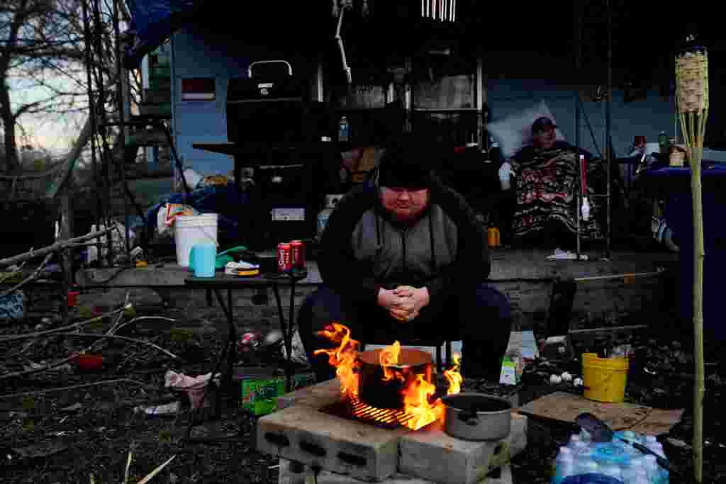 Christopher Bowlin, de 24 años, se sienta junto a un fuego fuera de su casa para hervir huevos y mantenerse caliente después del tornado, en Mayfield, Kentucky.