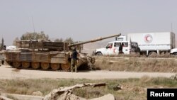 Un tanque del ejército sirio y un camión de la Luna Roja Creciente siria son vistos a la entrada de Harasta, en Ghouta, el suburbio este de Damasco, el jueves, 22 de marzo, de 2018.