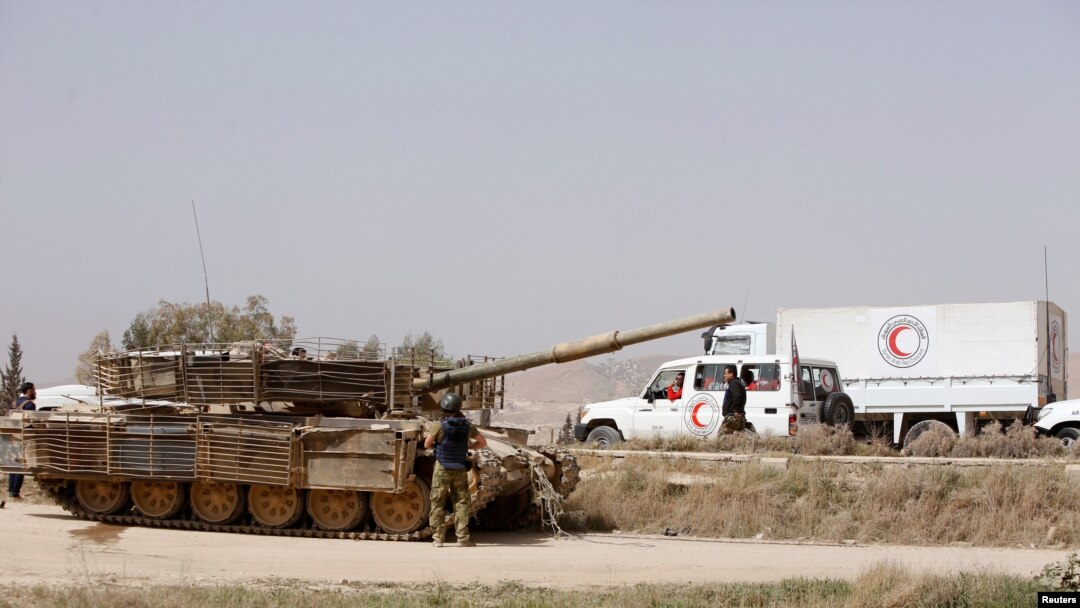 Tank militer milik tentara Suriah dan truk Bulan Sabit Merah Suriah berjaga di pintu masuk Harasta, pinggiran Damaskus, kawasan timur laut Ghouta, Suriah, 22 Maret 2018.
