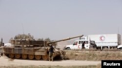 Tank militer milik tentara Suriah dan truk Bulan Sabit Merah Suriah berjaga di pintu masuk Harasta, pinggiran Damaskus, kawasan timur laut Ghouta, Suriah, 22 Maret 2018.