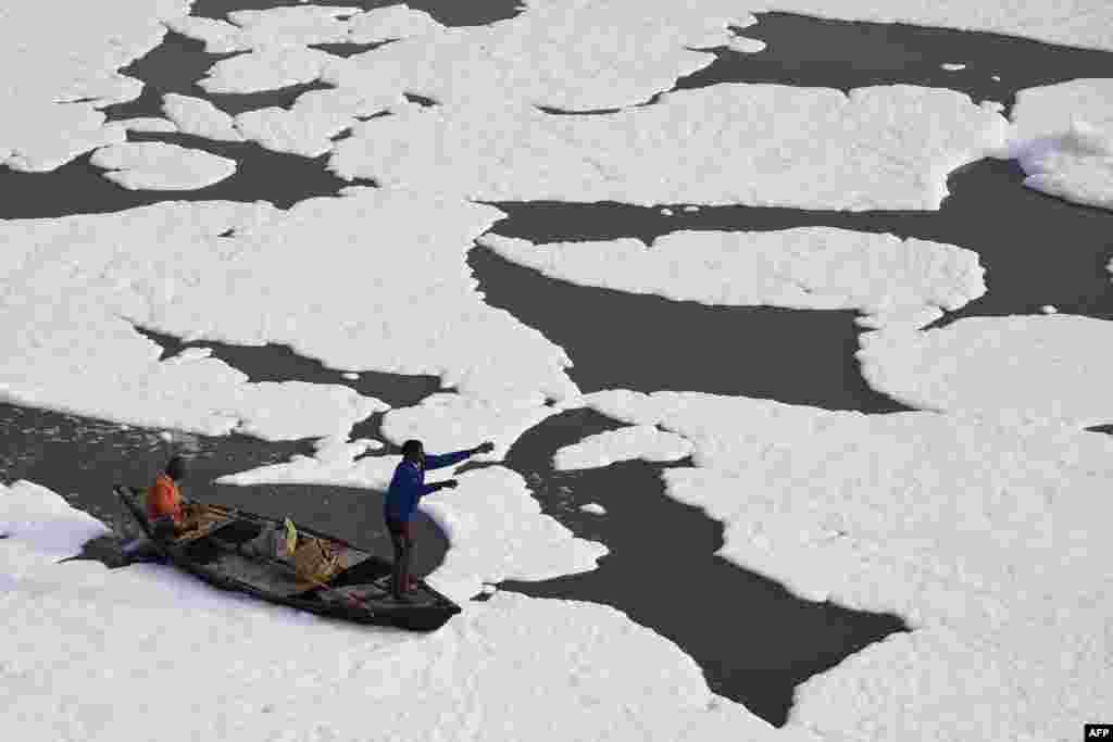 Men row a boat in the polluted waters of river Yamuna covered with foam in New Delhi, India.