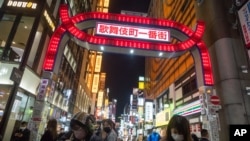People walk by a street filled with entertainment, restaurants and bars in the Shinjuku neighborhood of Tokyo, Japan, on April 9, 2021, as government announced it will raise the coronavirus alert level to allow tougher measures.