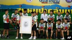 Coach Ekkapol Janthawong, left, and the 12 boys show their respect and thanks as they hold a portrait of Saman Gunan, the retired Thai SEAL diver who died during their rescue attempt, during a press conference in Chiang Rai, northern Thailand, Wednesday, July 18, 2018. (AP Photo/Vincent Thian)