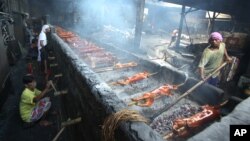 Filipino workers turn bamboo poles used in pigs at a roasting pit in suburban Quezon city, Philippines on Tuesday, Dec. 23, 2014.