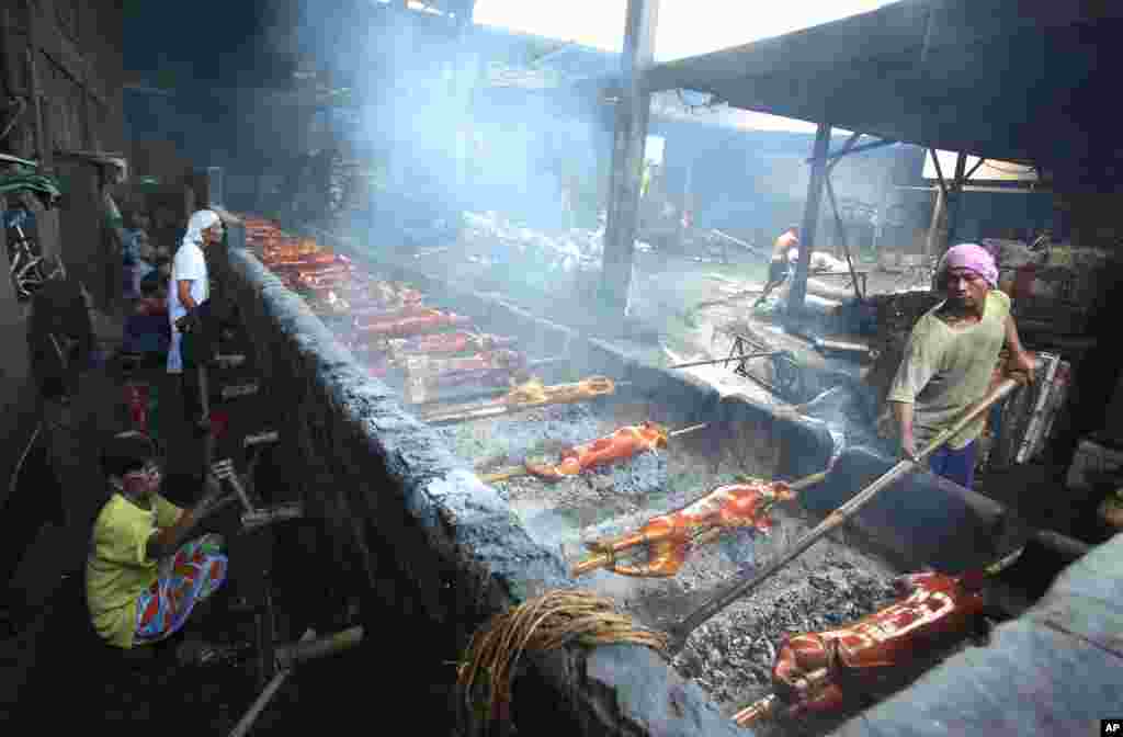 Des marchands de viande cuite philippins tournent des perches de bambou utilisés pour la cuisson du porc dans une fosse de torréfaction dans la banlieue de la ville de Quezon, aux Philippines, mardi 23 décembre 2014.