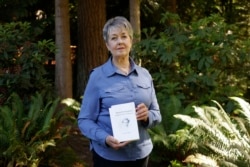 Karen McKnight stands in her backyard on Saturday, June 19, 2021, in Sammamish, Wash., holding two books written by her brother Ross Bagne of Cheyenne, Wyo. (AP Photo/John Froschauer)