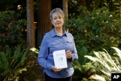 Karen McKnight stands in her backyard on Saturday, June 19, 2021, in Sammamish, Wash., holding two books written by her brother Ross Bagne of Cheyenne, Wyo. (AP Photo/John Froschauer)