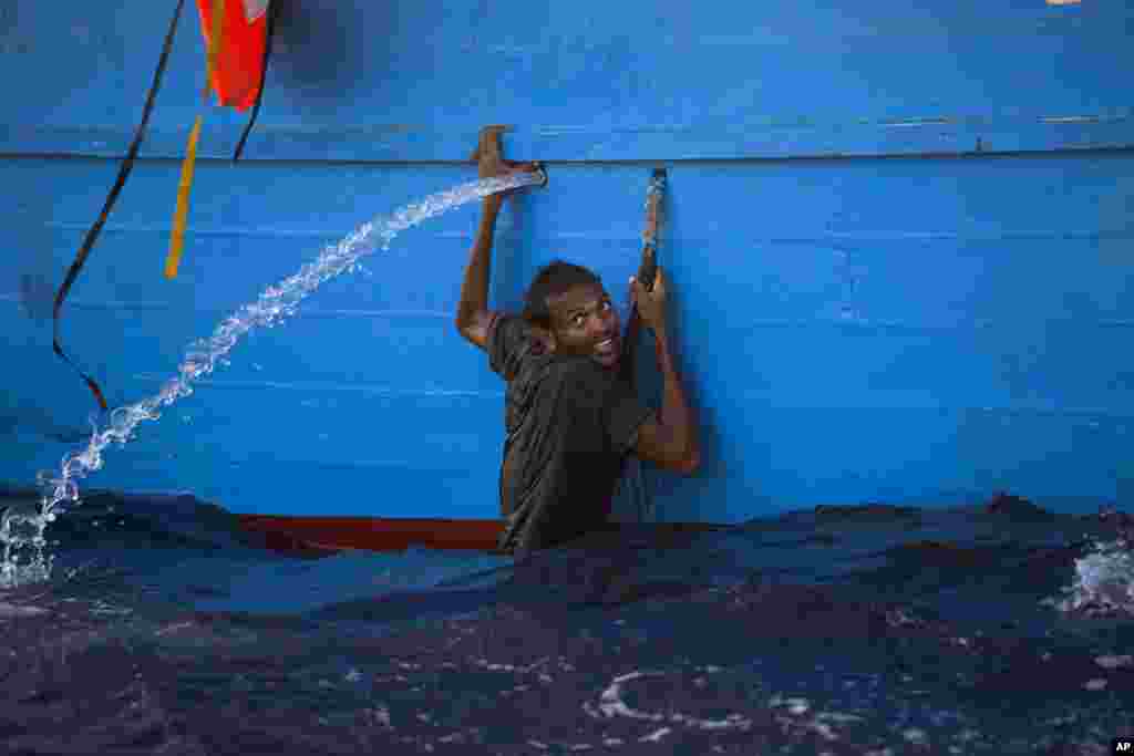 Seorang pria migran tampak bergantung di pinggiran perahu kayu di Laut Tengah, setelah melompat dari sebuah perahu yang penuh penumpang di lepas pantai Sabratha, Libya.