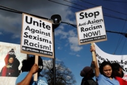 Demonstrators hold signs during a protest following the deadly shootings in Atlanta, Georgia, March 18, 2021.