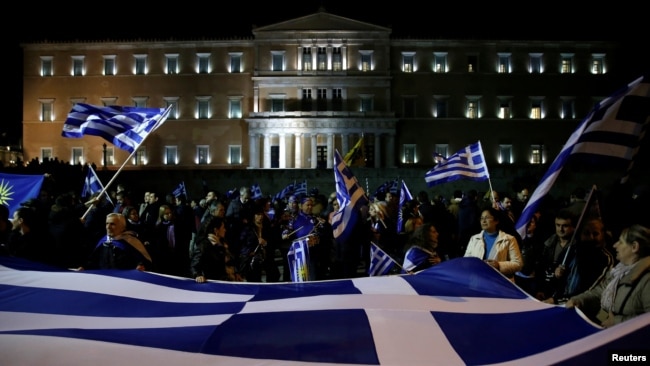 FILE - Protesters hold a giant Greek national flag during a demonstration against the agreement reached by Greece and Macedonia to resolve a dispute over the former Yugoslav republic's name, in front of the parliament building in Athens, Jan. 24, 2019.