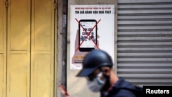 FILE - A man uses a smartphone as he walks past a poster warning against spreading 'fake news' on the coronavirus in Hanoi, Vietnam, April 14, 2020.