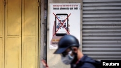 FILE - A man uses a smartphone as he walks past a poster warning against the spread of 'fake news' on the coronavirus, in Hanoi, Vietnam April 14, 2020. 