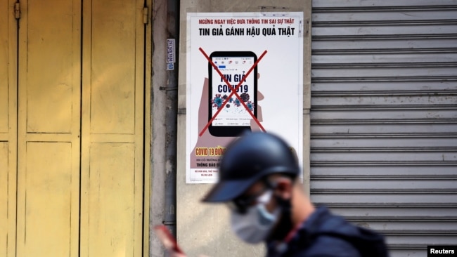 FILE - A man uses a smartphone as he walks past a poster warning against the spread of 'fake news' on the coronavirus, in Hanoi, Vietnam April 14, 2020.