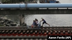 In this Wednesday, Aug. 12, 2015 photo, a man pushes a metal-wheeled cart with benches fashioned from scrap wood as he ferries passengers for 10 pesos each along the railway in Manila. (AP Photo/Aaron Favila)