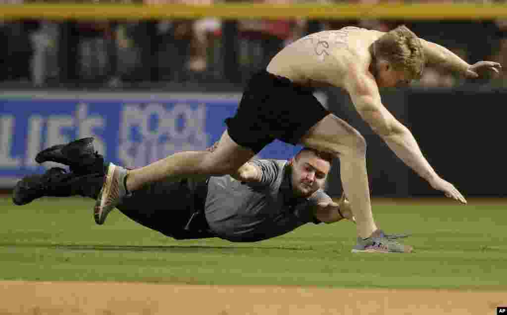 A fan, top, is tackled by security after running onto the field during the third inning of a baseball game between the Colorado Rockies and the Arizona Diamondbacks in Phoenix.
