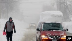 A man walks with a gas can along Como Park Boulevard in Lancaster, N.Y., as he looks at a minivan go by with snow on its roof, Nov. 20, 2014.