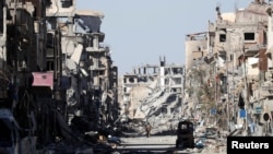 FILE - A fighter of Syrian Democratic Forces stands amid the ruins of buildings near the Clock Square in Raqqa, Syria, Oct. 18, 2017.