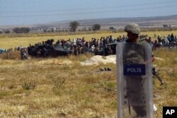 Turkish soldiers stand as people from the Syrian town of Ain al-Arab, or Kobani, wait to cross into Turkey following the attacks by Islamic State militants as seen from the Turkish side of the border in Suruc, Turkey, June 25, 2015.