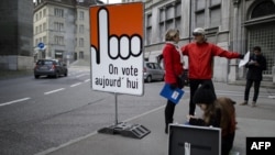 People stand next to a board reading in French "We vote today" in the old town section of Fribourg, Switzerland, Nov. 30, 2014. 