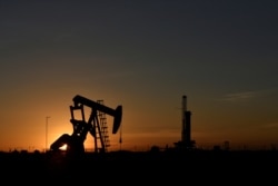 Pompa angguk beroperasi di depan rig pengeboran saat matahari terbenam di ladang minyak di Midland, Texas AS 22 Agustus 2018. (Foto: REUTERS/Nick Oxford)