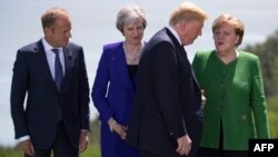 European Council President Donald Tusk,from left, British Prime Minister Theresa May and German Chancellor Angela Merkel look on as U.S. President Donald Trump arrives for the group photo at the G-7 Summit, June 8, 2018. 