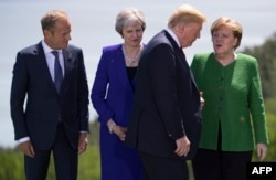 European Council President Donald Tusk,from left, British Prime Minister Theresa May and German Chancellor Angela Merkel look on as US President Donald Trump arrives for the group photo at the G7 Summit, June 8, 2018.
