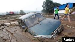 People walk past a car stranded in mud after heavy rainfalls hit Fushun, Liaoning province, August 17, 2013. 