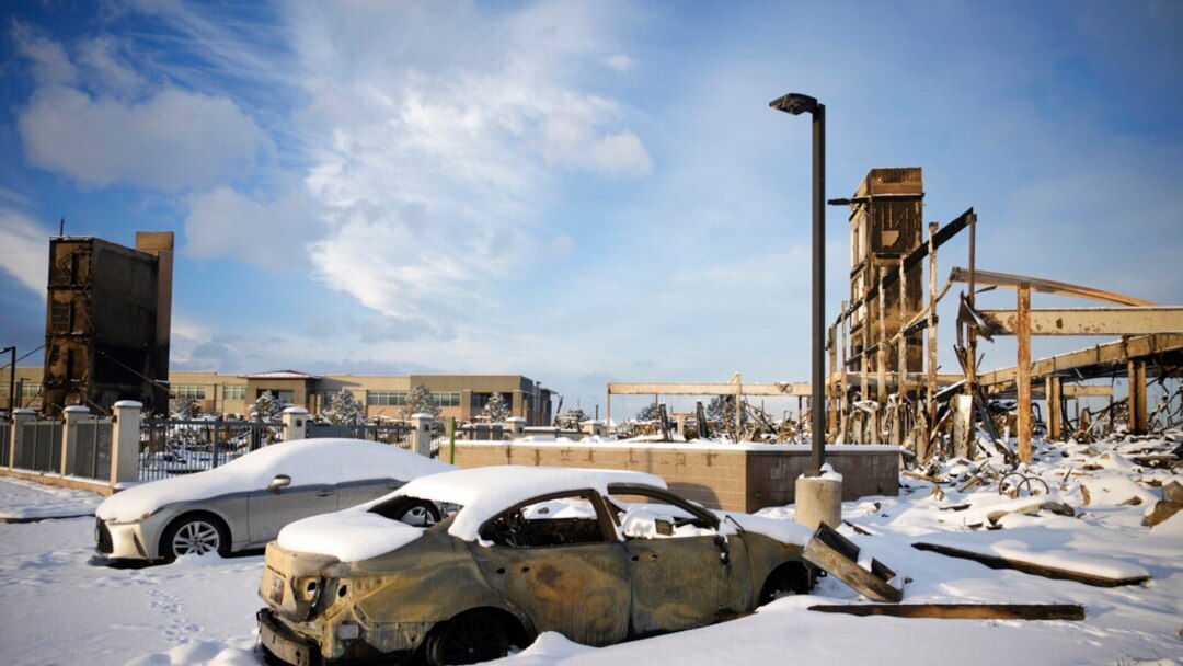 Snow left by a fast-moving winter storm covers the charred remains of a vehicle destroyed by wildfires in the parking lot of the Element hotel, which was also burned, Jan. 6, 2022, in Superior, Colo.