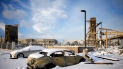 Snow left by a fast-moving winter storm covers the charred remains of a vehicle destroyed by wildfires in the parking lot of the Element hotel, which was also burned, Jan. 6, 2022, in Superior, Colo.