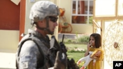 A US soldier attached to the Golden Lions forces walks past a girl carrying her doll, during a patrol in the city of Kirkuk, July 20, 2011