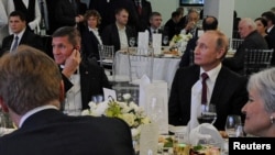 ປະທານາທິບໍດີ Vladimir Putin (ຂວາ) ນັ່ງ​ຢູ່​ຂ້າງໆ ນາຍ​ພົນ​ເບ້ຍ​ບຳນານ Michael Flynn (ຊ້າຍ) ​ໃນ​ຂະນ່ະພວກ​ທ່ານ​ເຂົ້າ​ຮ່ວມ​ໃນ​ການສະ​ແດງ ຄົບຮອບ 10 ປີ ຂອງ​ລາຍການ​ໂທລະພາບ (Russia Today) ຊຶ່ງ​ເປັນ​ຊ່ອຍ​ຂ່າວ​ໃນ Moscow, ຣັ​ດ​ເຊຍ, 10 ທັນວາ, 2015.