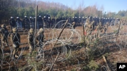 Polish police and border guards stand near the barbed wire as migrants from the Middle East and elsewhere gather at the Belarus-Poland border near Grodno Grodno, Belarus, Nov. 9, 2021. (Leonid Shcheglov/BelTA via AP)