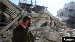 A Free Syrian Army fighter carries his weapon as he walks past damaged buildings in the Arabeen neighborhood of Damascus, Syria, Feb. 12, 2013.