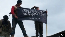 FILE - Rebels from al-Qaida-affiliated Jabhat al Nusra, also known as the Nusra Front, wave their brigade flag, as they step on the top of a Syrian air force helicopter at Taftanaz air base, Jan. 11, 2013.
