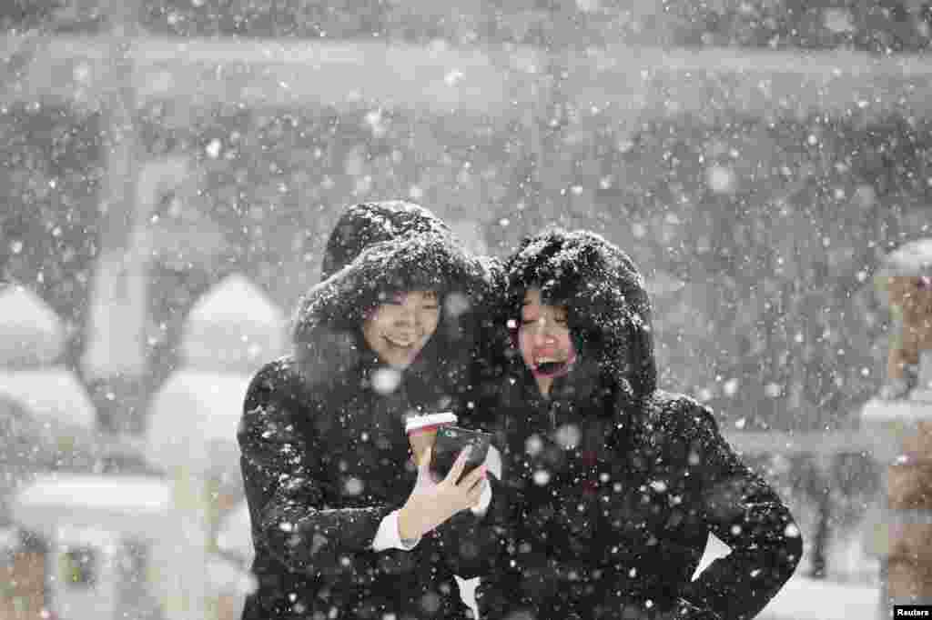 Women smile as they look at a picture on a mobile phone during snowfall in winter in central Seoul, South Korea.