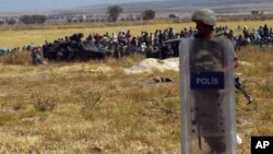 Turkish soldiers stand as people from the Syrian town of Kobani wait to cross into Turkey following the attacks by Islamic State militants as seen from the Turkish side of the border in Suruc, Turkey, June 25, 2015. 