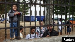 Refugees look through the fence around the asylum processing center in Traiskirchen, Austria, Aug. 17, 2015. 