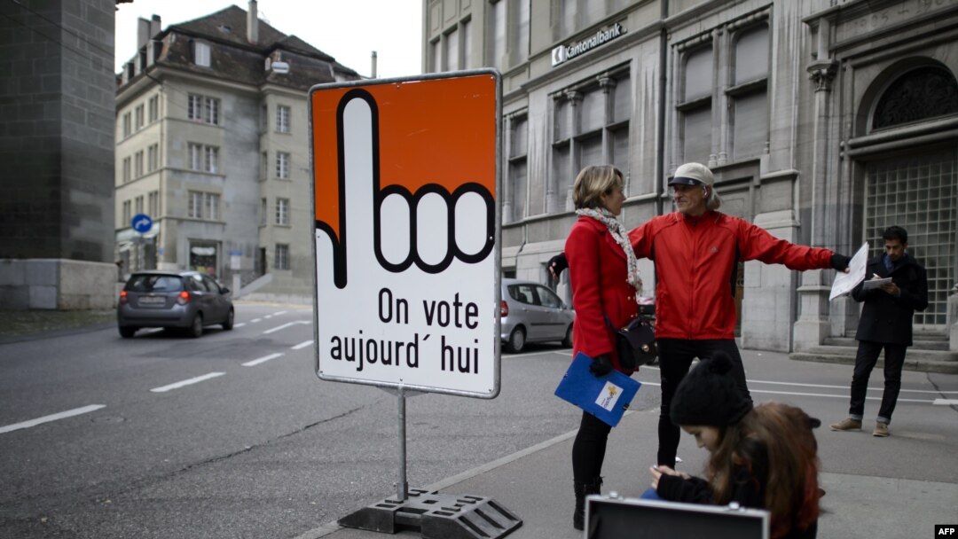Orang-orang berdiri di papan bertuliskan "Kami memilih hari ini" dalam bahasa Perancis di kota tua Fribourg, Swiss, 30 November 2014. 