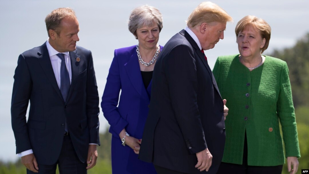 European Council President Donald Tusk,from left, British Prime Minister Theresa May and German Chancellor Angela Merkel look on as U.S. President Donald Trump arrives for the group photo at the G-7 Summit, June 8, 2018. 