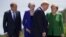 European Council President Donald Tusk,from left, British Prime Minister Theresa May and German Chancellor Angela Merkel look on as U.S. President Donald Trump arrives for the group photo at the G-7 Summit, June 8, 2018. 